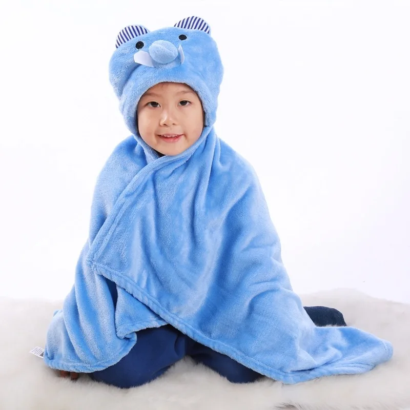 Un niño pequeño sentado sobre una superficie blanca, envuelto en una manta azul con una capucha con orejas, lo que le da la apariencia de un lindo animal o personaje. El niño sonríe y parece disfrutar del acogedor y divertido atuendo.