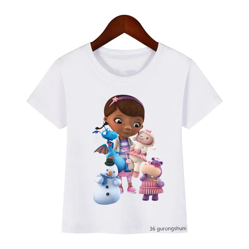 Una camiseta blanca con un estampado gráfico. El estampado presenta una ilustración estilo caricatura de una joven con cabello castaño y una diadema morada, que lleva un vestido rosa.