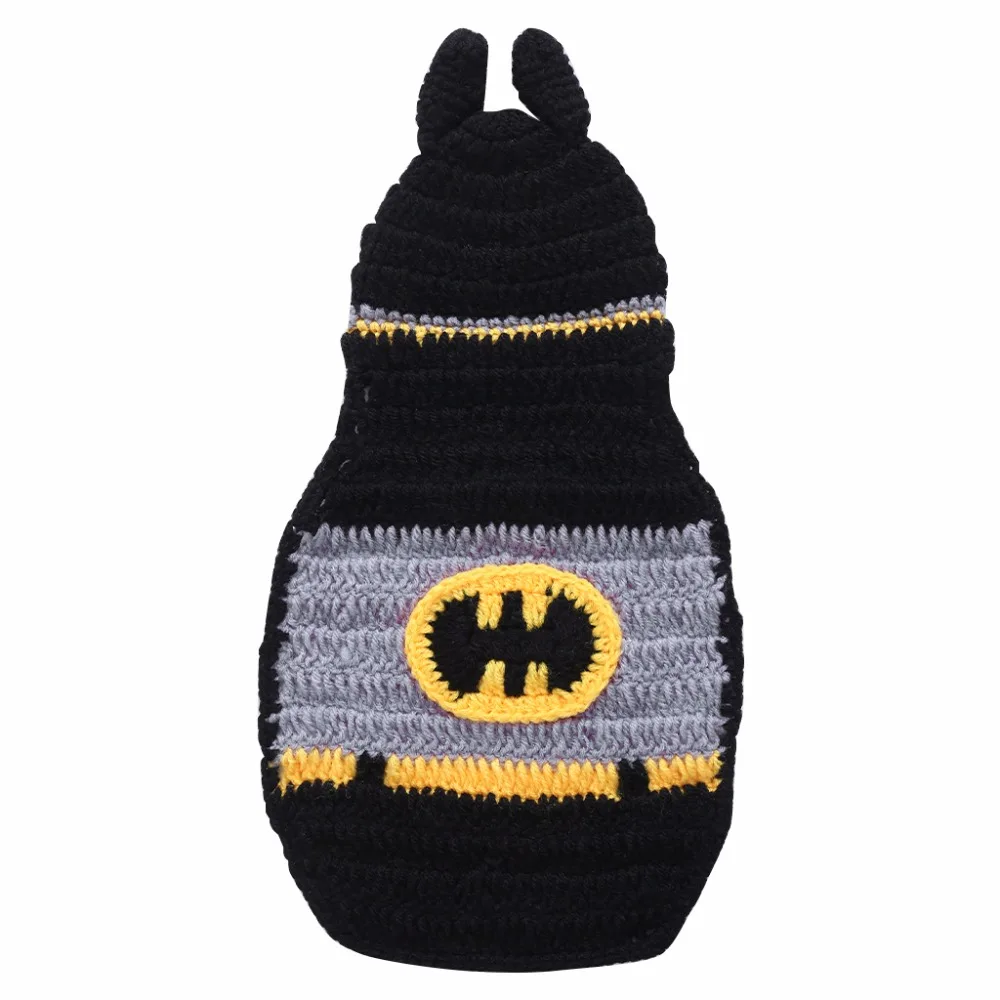 Un gorro tejido a crochet o tejido con un diseño que se asemeje al logo de Batman. El sombrero es predominantemente negro con un emblema de Batman amarillo y negro en el centro y tiene dos orejas pequeñas y puntiagudas en la parte superior.