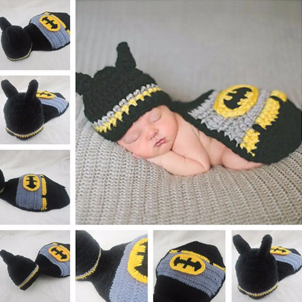 Un bebé vestido con un conjunto de temática de Batman, que incluye gorro y manta. El sombrero tiene el logo de Batman y la manta está diseñada para parecerse a la capa de Batman, completa con el logo de Batman.