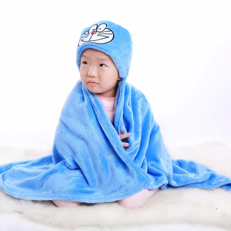 Un niño pequeño envuelto en una manta azul con una capucha que tiene la cara de un personaje. El niño parece estar sentado sobre una superficie blanda, posiblemente una cama o un cojín, y mira ligeramente hacia un lado con expresión neutra.