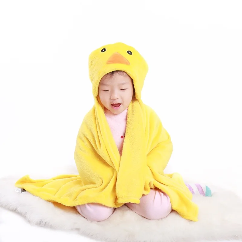 Un niño pequeño sentado sobre una superficie blanda, posiblemente una manta o un cojín. El niño lleva una bata amarilla con una capucha que tiene un diseño de cara de pato, dando la impresión de un lindo patito.