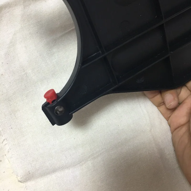 Un objeto negro con un botón rojo en el extremo, que parece ser parte de un dispositivo o herramienta. El objeto tiene una forma rectangular con una serie de crestas o ranuras a lo largo de su longitud, lo que sugiere que podría estar diseñado para agarrar o asegurar algo.