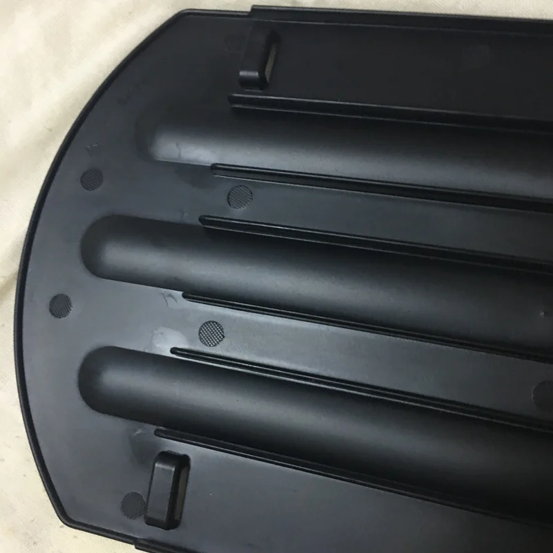 Un objeto de plástico negro con una serie de crestas o ranuras, que podría ser parte de un dispositivo o electrodoméstico más grande. Parece ser un componente con una manija en el lado derecho, posiblemente para abrir o ajustar el dispositivo.