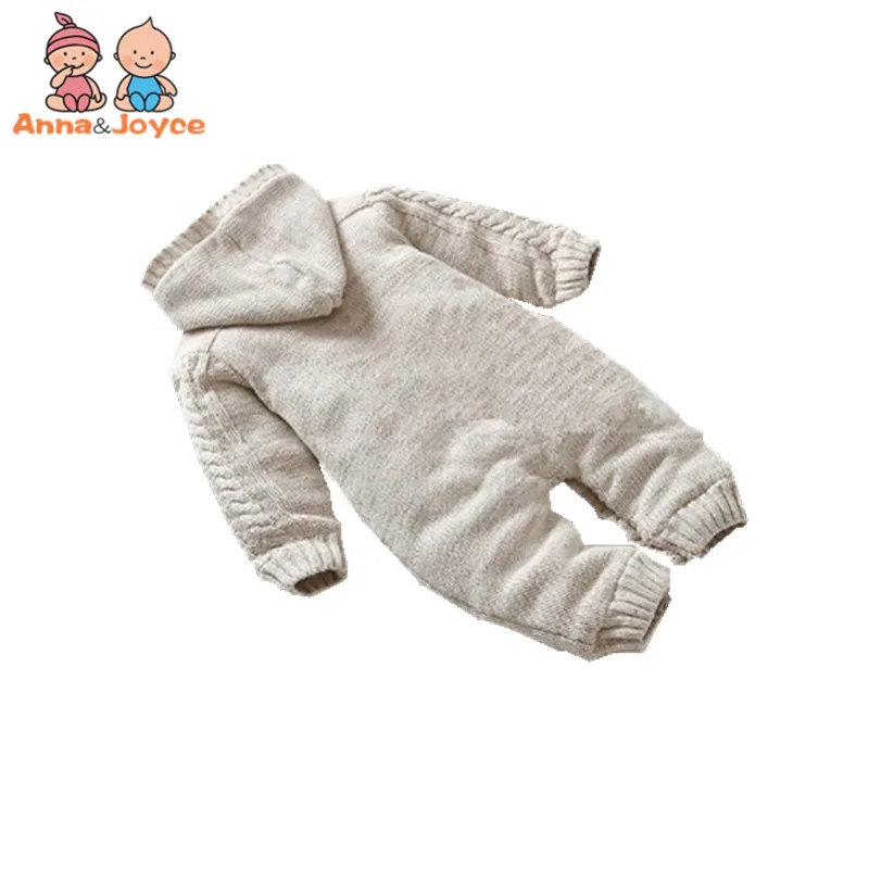 Un mono de bebé. Parece ser de color claro, posiblemente beige o crema, con capucha y puños y tobillos de canalé. El mono tiene una cremallera frontal y parece estar diseñado para brindar calidez y comodidad, probablemente para climas más fríos.