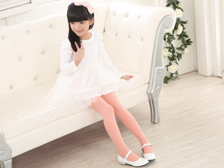 Una niña con un vestido blanco y zapatos blancos se sienta en un sofá blanco
