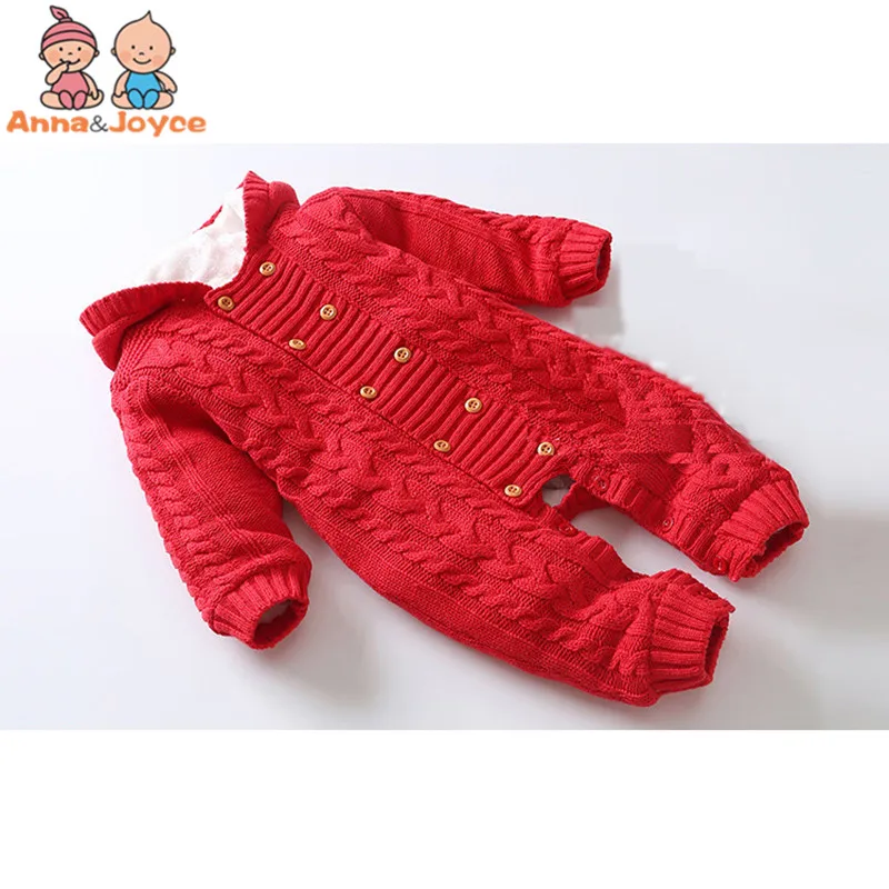 Un mono de punto rojo con capucha. Parece estar diseñado para un bebé o un niño pequeño, dado el tamaño y el estilo. El mono tiene cuello, puños y dobladillo de canalé y cuenta con una serie de botones en la parte delantera para cerrarlo.