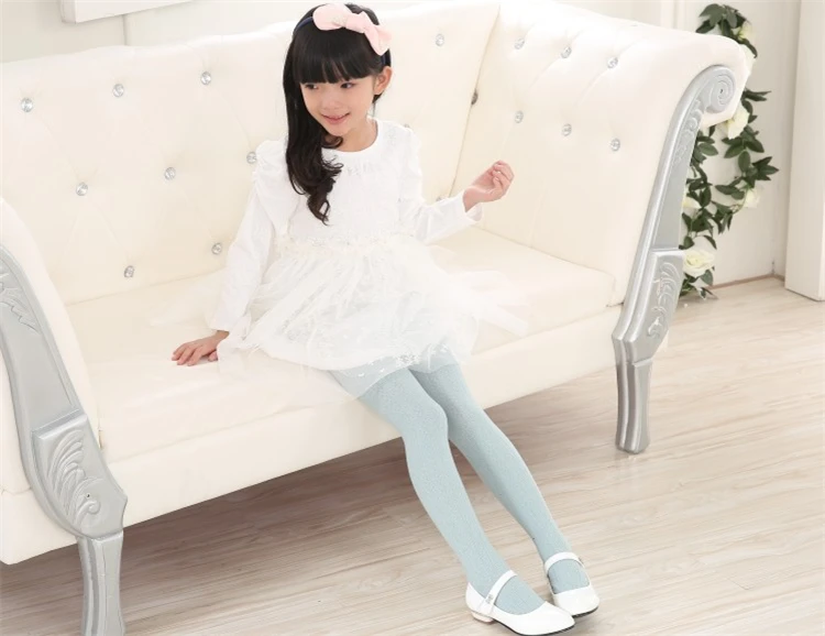Una niña con un vestido blanco y medias azules se sienta en un sofá blanco
