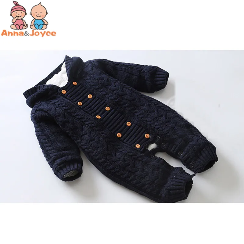 Un mono de bebé. Es una prenda de color azul oscuro con textura de canalé y capucha. El mono tiene cierre de botón y parece estar diseñado para un recién nacido o un bebé pequeño.