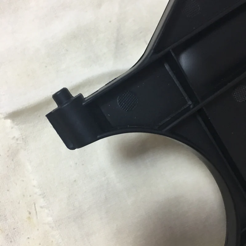 Un primer plano de un objeto negro con forma curva, que parece ser parte de un objeto más grande. Parece que podría ser un componente de un mueble, posiblemente una silla o un sofá, dadas las bisagras visibles y el material similar a la tela en el fondo.