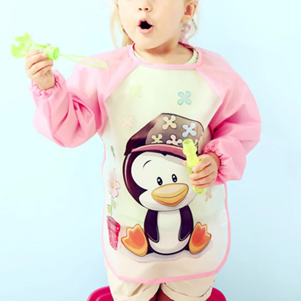 Un niño pequeño con un pijama rosa y blanco con un diseño de pingüino en la parte delantera. El niño sostiene un objeto verde en su mano derecha, que parece ser un juguete o un objeto pequeño.