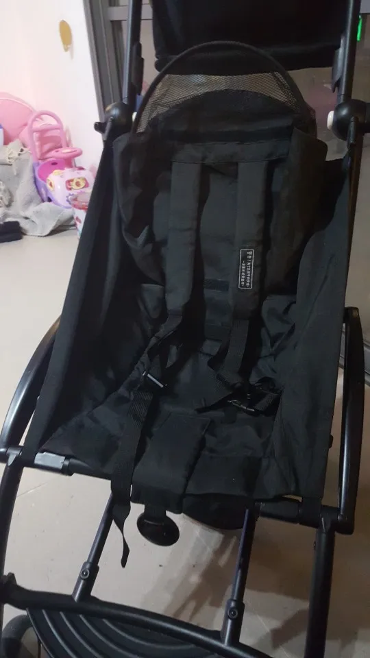 Un cochecito negro con capota de malla. El cochecito parece estar diseñado para un niño, con un asiento que actualmente está vacío. El cochecito tiene una estructura y ruedas negras y parece que está diseñado para uso en exteriores, posiblemente para caminar o trotar.