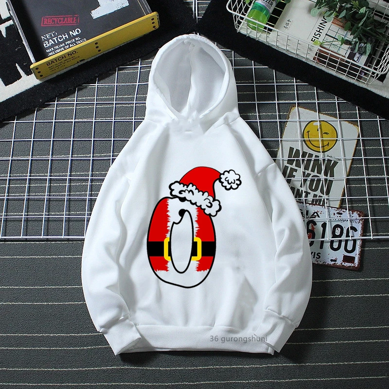 Una sudadera con capucha blanca con un diseño gráfico en el frente. El diseño presenta una representación estilizada de un árbol de Navidad con una base a rayas rojas y amarillas, rematado con un copo de nieve blanco.