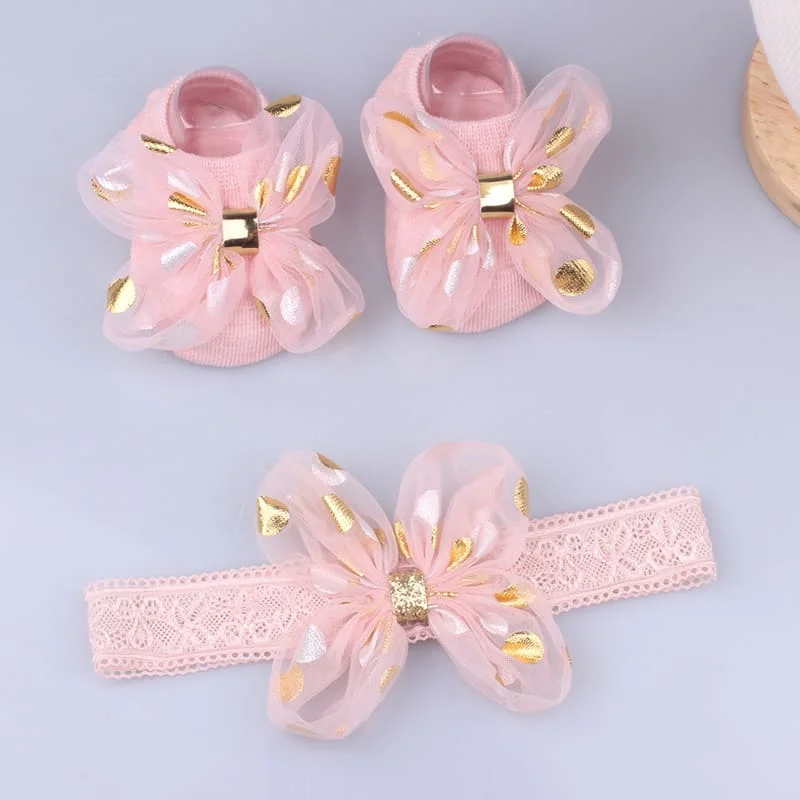 Un par de zapatos de bebé rosa con acentos dorados y un arco rosa a juego