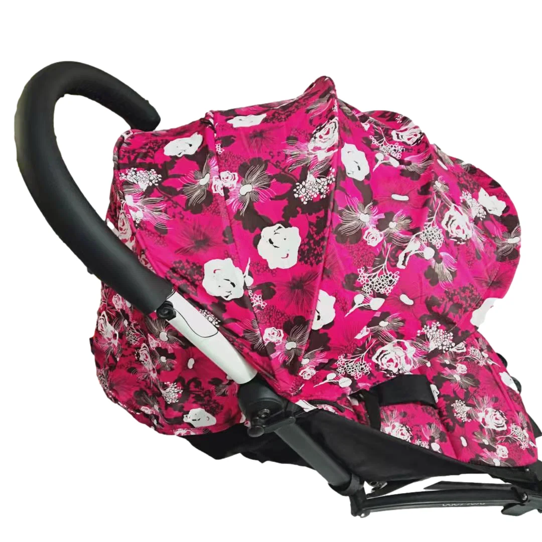 Un cochecito con capota que tiene un estampado floral. El cochecito parece estar diseñado para un niño, con un marco negro y un dosel floral rosa y blanco. La capota está diseñada para proporcionar sombra y protección de los elementos al niño sentado en el cochecito.