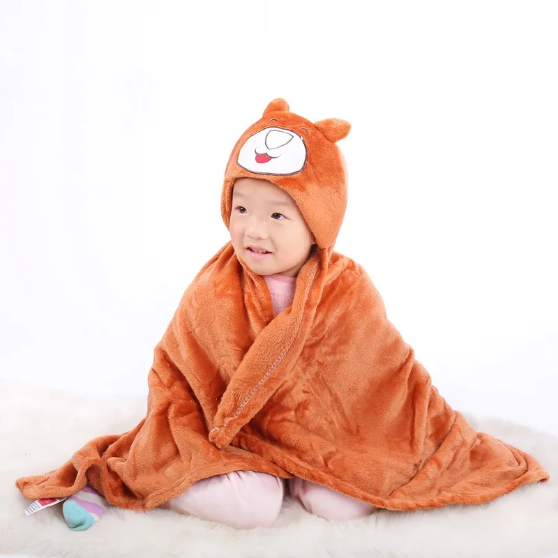 Un niño pequeño sentado sobre una superficie suave, envuelto en una acogedora manta naranja. El niño lleva un sombrero con una linda cara de animal, que parece ser un oso o una criatura similar.