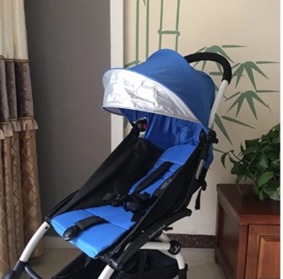 Un cochecito azul y negro con capota. El cochecito parece estar diseñado para un niño, con un asiento reclinable y un asa para empujar. Está en el interior y hay una planta y un mueble al fondo.
