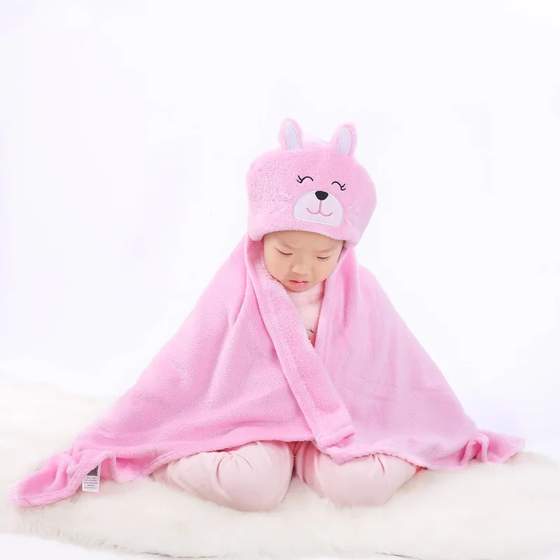 Un bebé envuelto en una manta rosa con una capucha que tiene un lindo diseño de conejito. El bebé está sentado sobre una superficie blanca y la escena general es muy suave y de colores pastel, lo que le da una apariencia gentil y adorable.