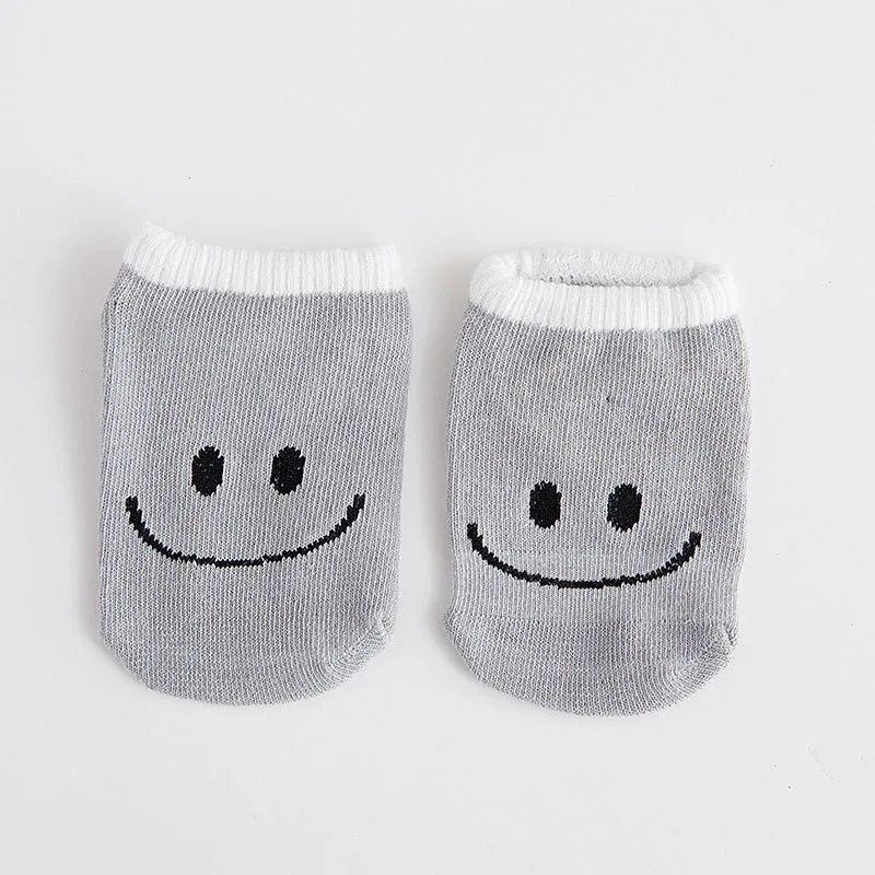 Dos pares de calcetines con un diseño de carita sonriente. Los calcetines son grises con un ribete blanco alrededor de los bordes superior e inferior. Los rostros son simples, con dos puntos por ojos y una línea curva por boca, lo que les da una apariencia alegre.