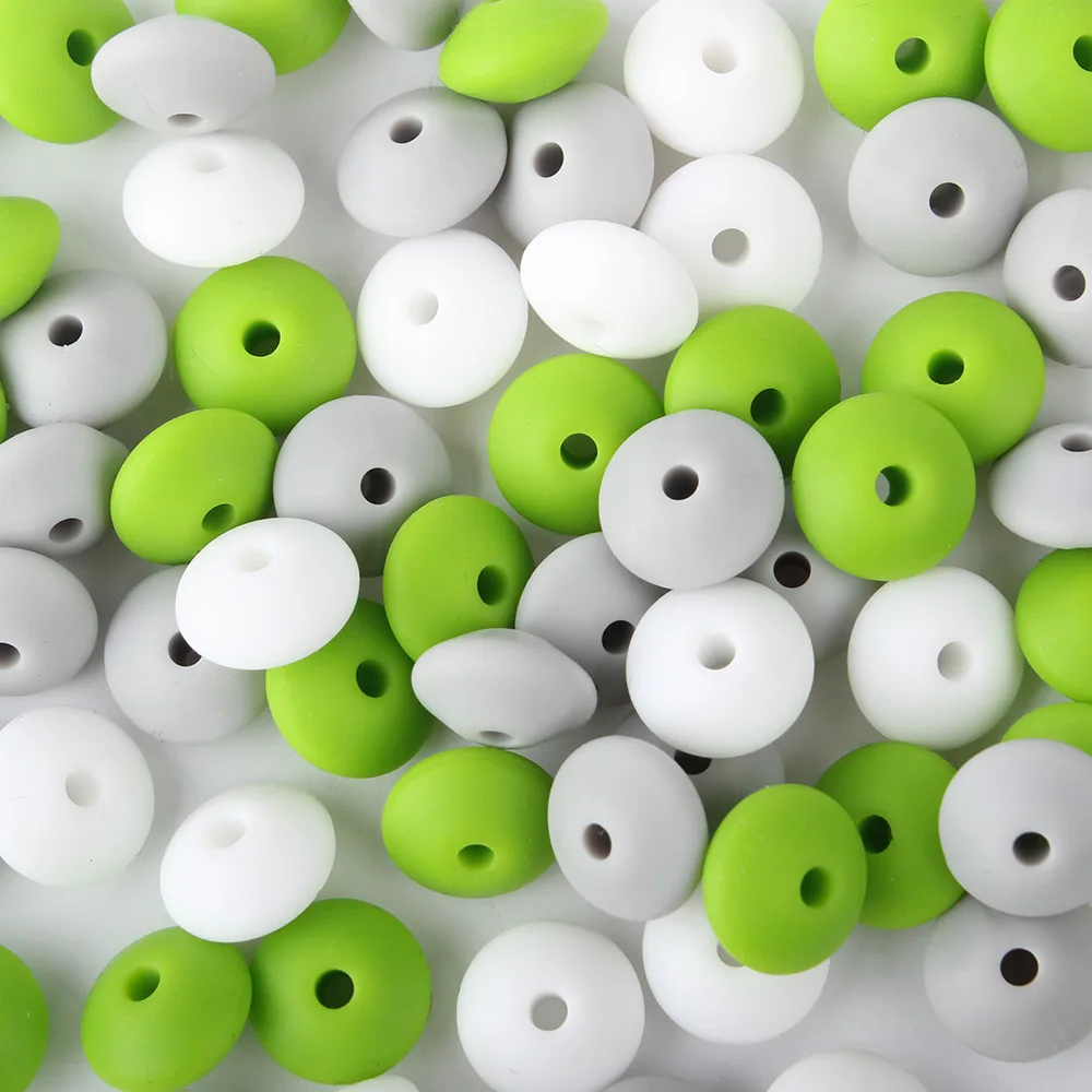 Una colección de objetos pequeños y redondos que parecen cuentas o espaciadores. Están coloreados en dos tonos, verde y blanco, y tienen un agujero en el centro, lo que sugiere que están diseñados para ser ensartados, posiblemente para hacer joyas u otras manualidades.