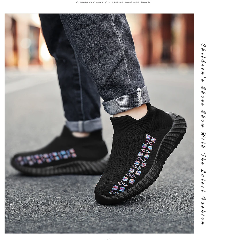 Una persona que lleva un par de zapatillas negras con suela texturizada. Las zapatillas tienen un patrón colorido en el lateral, que parece ser una serie de pequeños adornos o parches de forma cuadrada.