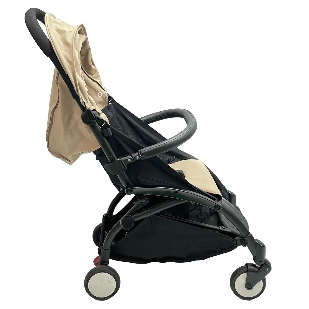 Silla de paseo con estructura negra y tela beige o de color claro. El cochecito parece estar diseñado para un solo niño y tiene un dosel que se puede extender para brindar sombra al niño.