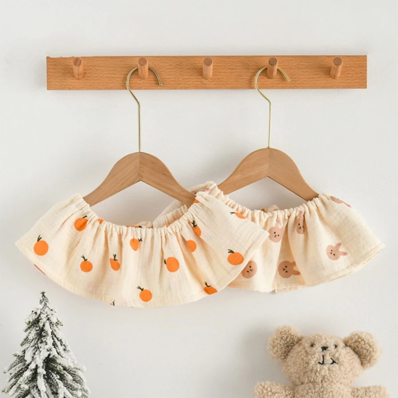 Una percha de madera con una falda colgando. La falda tiene un dobladillo con volantes y está adornada con un patrón de calabazas naranjas y hojas marrones, lo que sugiere un tema otoñal o otoñal.
