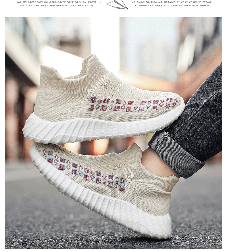 Un par de zapatillas con suela blanca y parte superior en color crema. Las zapatillas tienen un diseño estampado en el lateral, que parece ser un motivo geométrico o tribal. La persona que lleva las zapatillas solo es visible parcialmente, centrándose en los propios zapatos.