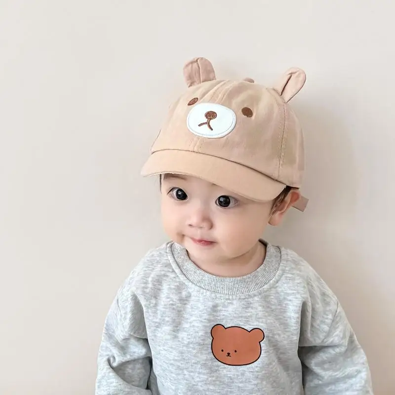 Un bebé con un sombrero y una camisa con un oso de peluche