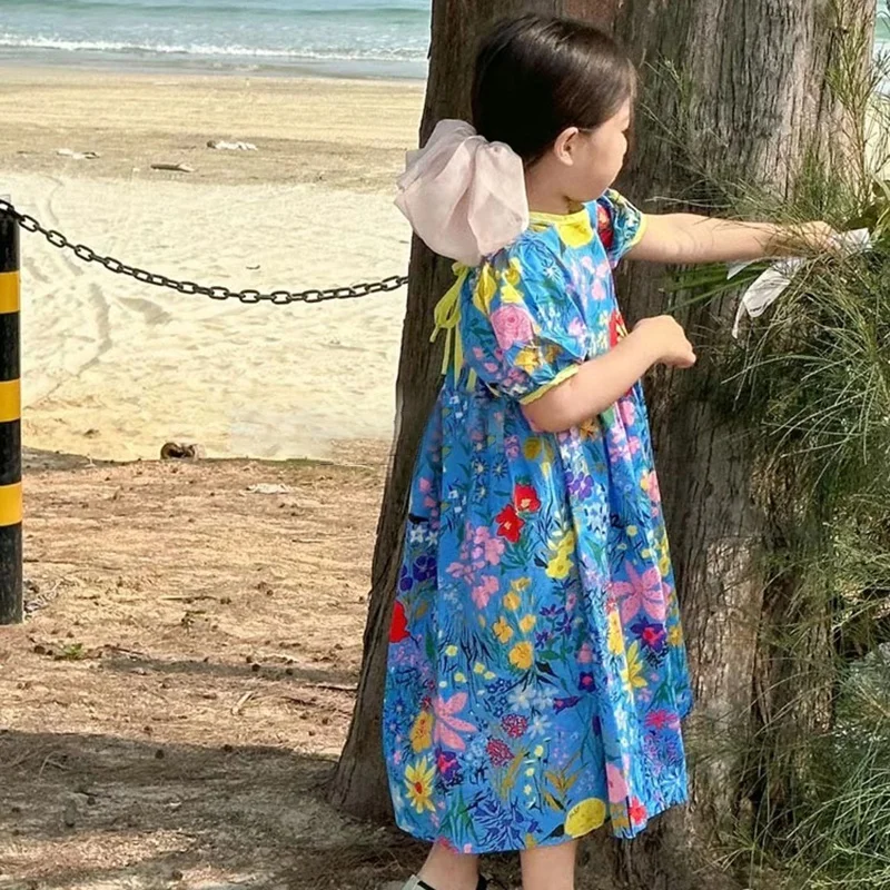 Una niña con un vestido azul está parado junto a un árbol
