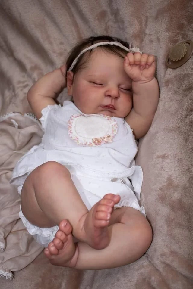 Un bebé con un vestido blanco y una diadema está durmiendo en una manta