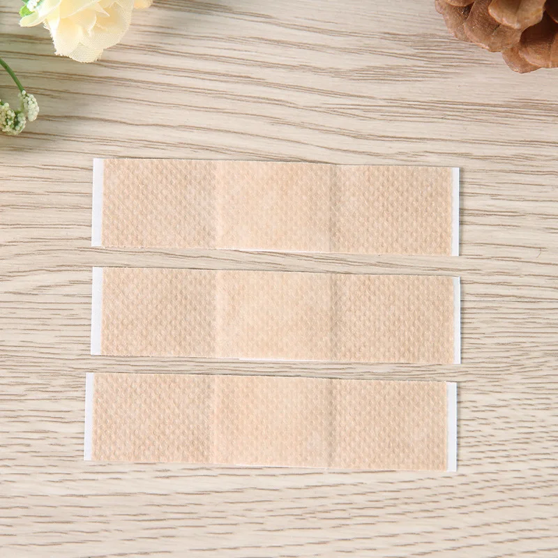 Un conjunto de vendas adhesivas colocadas sobre una superficie de madera. Hay tres vendajes en total, cada uno con un adhesivo blanco y una almohadilla absorbente de color beige o marrón claro. Los vendajes están diseñados para cubrir y proteger heridas o cortes menores.