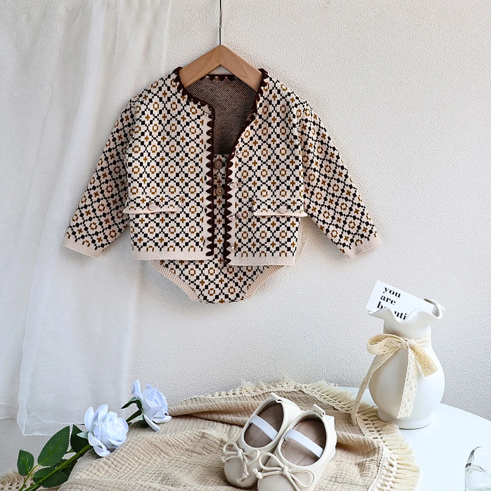 Una chaqueta de bebé blanca cuelga de una percha junto a un par de zapatos de bebé