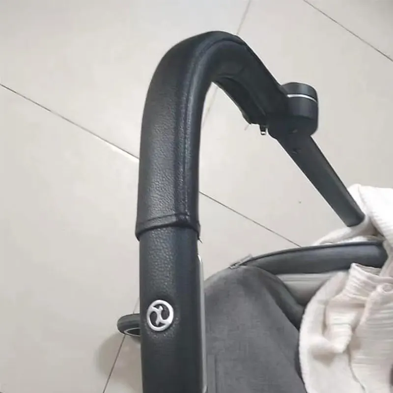 Un primer plano de un manillar negro, que parece ser parte de un cochecito o un tipo similar de cochecito de bebé.