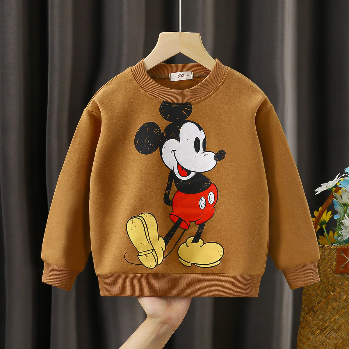 Una persona sostiene un suéter marrón con un mouse de Mickey