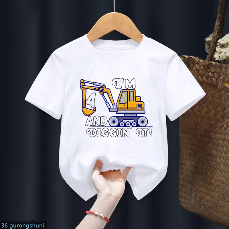Una camiseta blanca con un diseño gráfico. El diseño presenta una ilustración estilo dibujos animados de una excavadora amarilla con el texto ¡TENGO 4 Y LO ESTOY DIGGIN'! alrededor