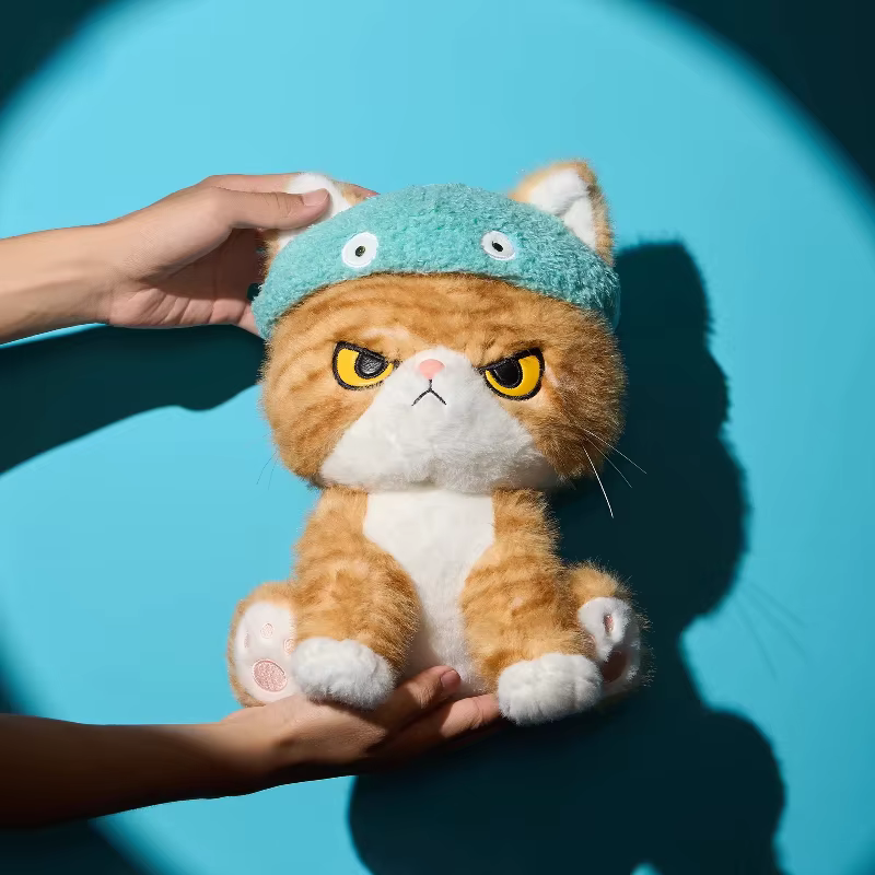 Peluche de gato naranja con expresión divertida, almohada