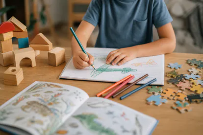 Materiales de dibujo, bloques, rompecabezas y un libro en una mesa infantil.