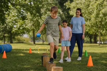 Niños jugando con pelota y circuito de equilibrio en un parque seguro.